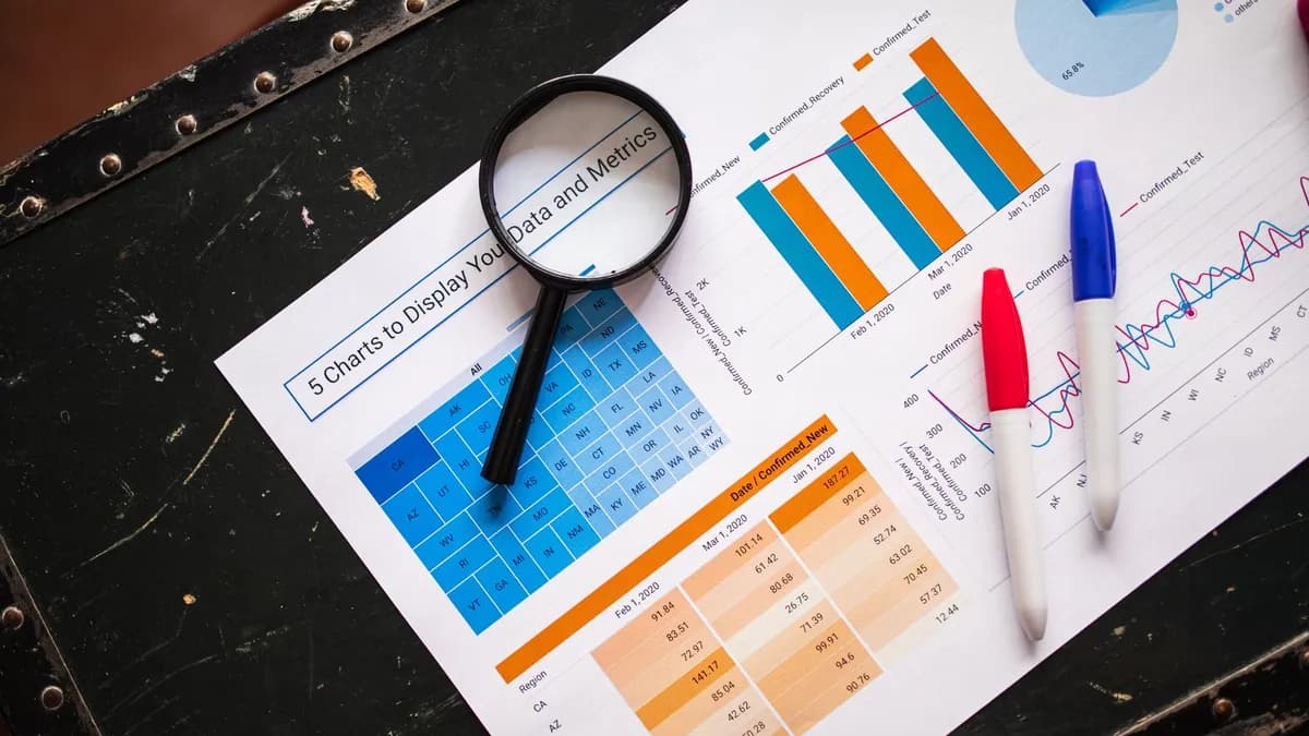 Flat lay of business charts and graphs with magnifying glass and markers on a dark surface.