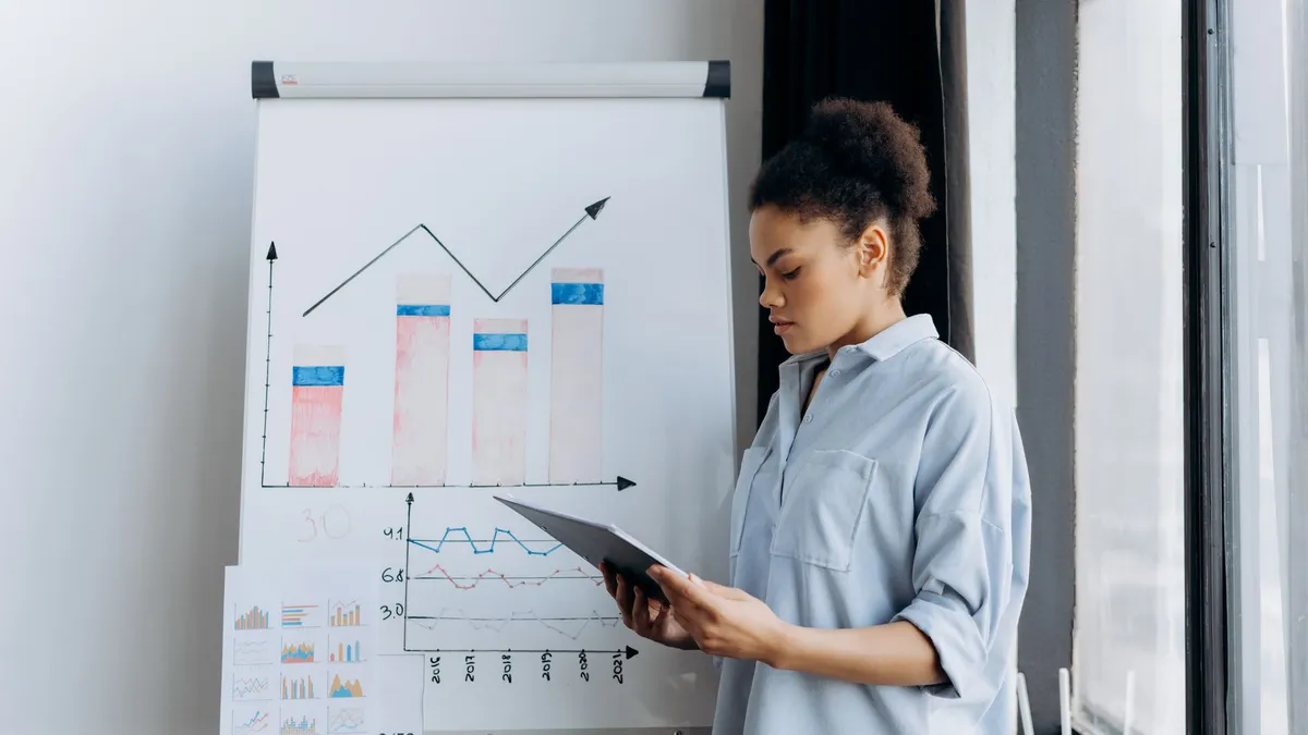 A woman analyzing sales data on a tablet next to a presentation board with graphs.