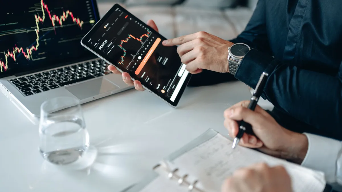 Two professionals analyzing stock graphs on digital devices in a modern business setting.