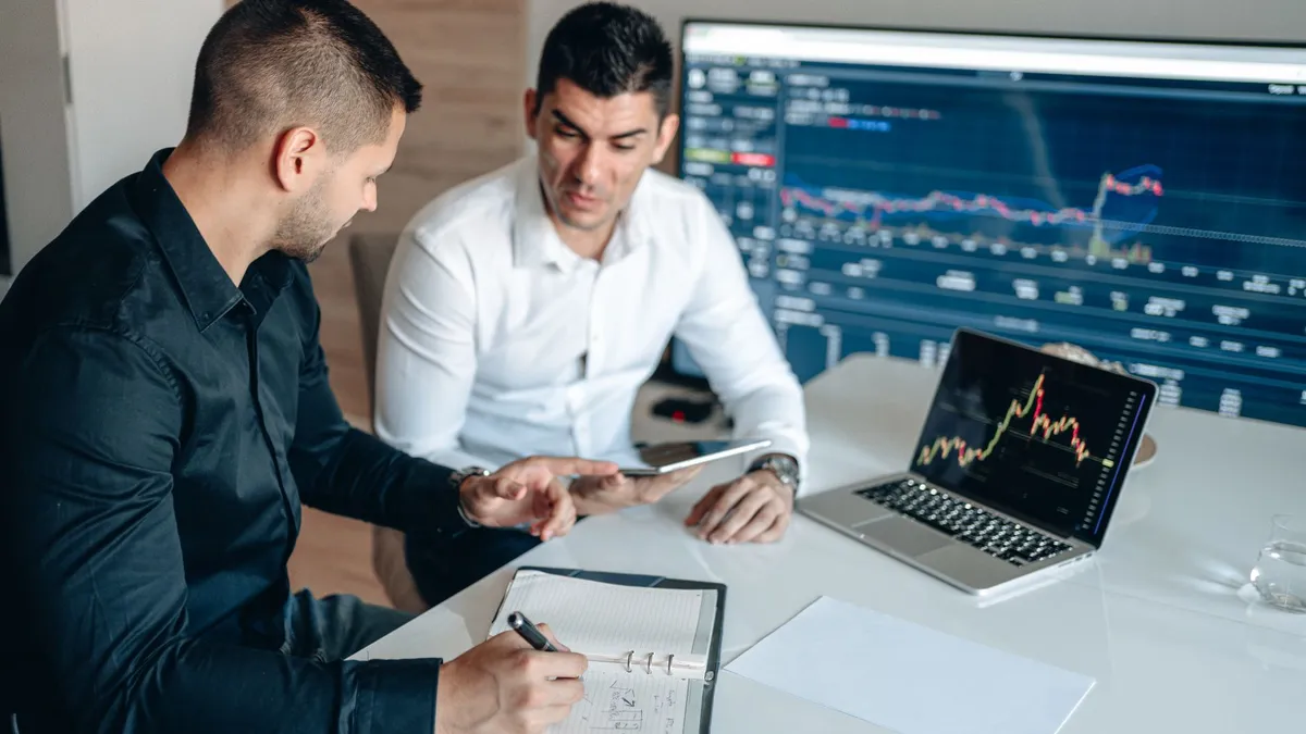 Two businessmen analyzing financial data on digital screens during a collaborative meeting.