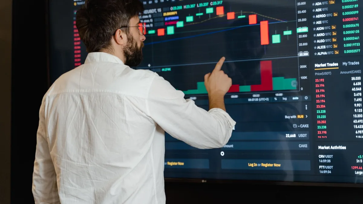 A man analyzes cryptocurrency graphs on a touchscreen monitor in a modern office setting.