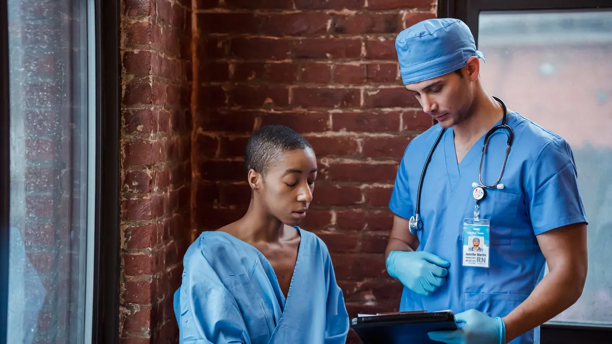 Pensive man nurse in blue uniform standing and demonstrating diagnosis to serious African American female patient in hallway of hospital in daytime