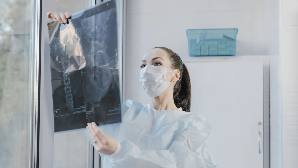 A medical professional examining an X-ray near a window in a clinical setting.