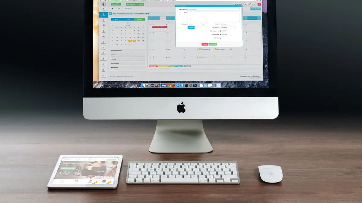 A sleek office setup featuring an Apple iMac, iPad, and keyboard on a wooden desk.