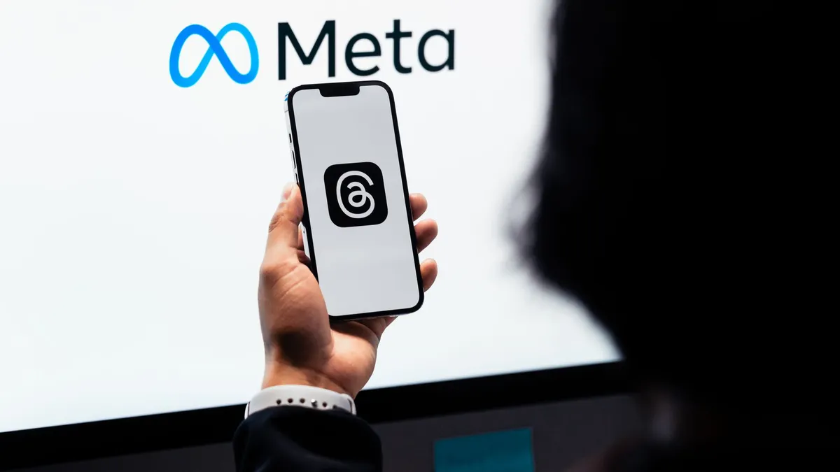 Hands holding smartphone with Meta Threads logo on screen, Meta branding in background.