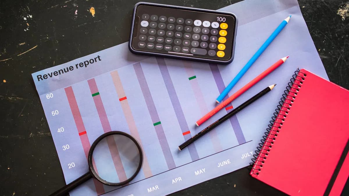 Flat lay of revenue report with a calculator, pencils, and notebook.