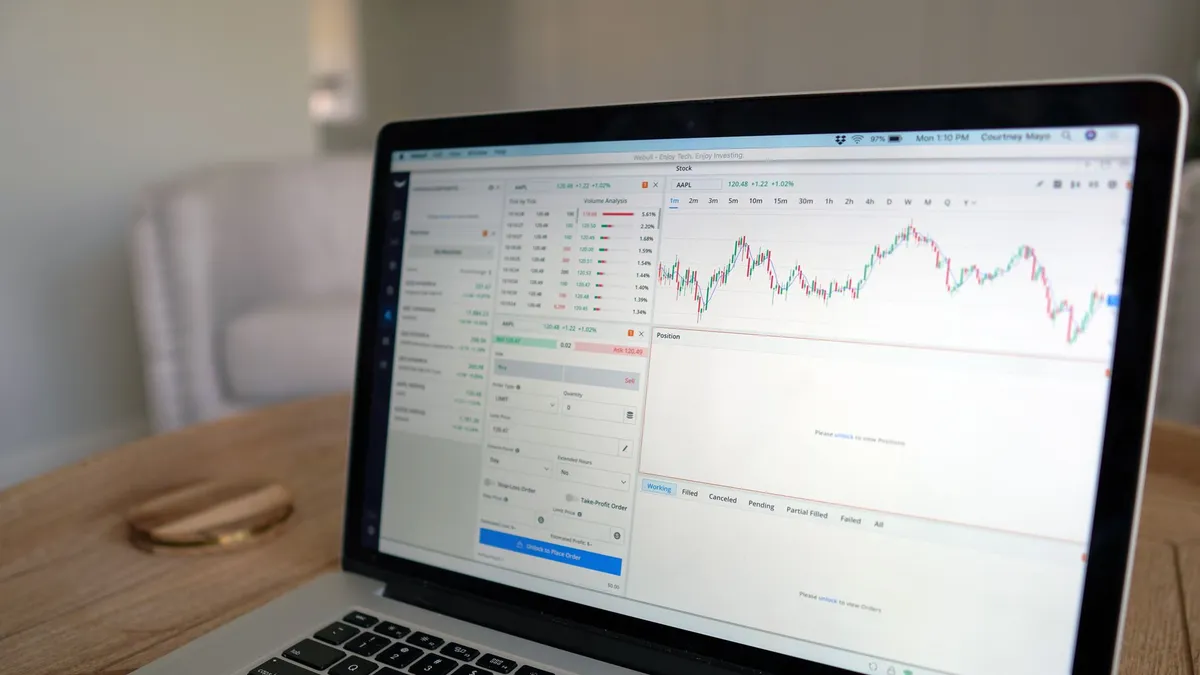 Close-up of a laptop displaying stock trading software with a market chart on a wooden table.