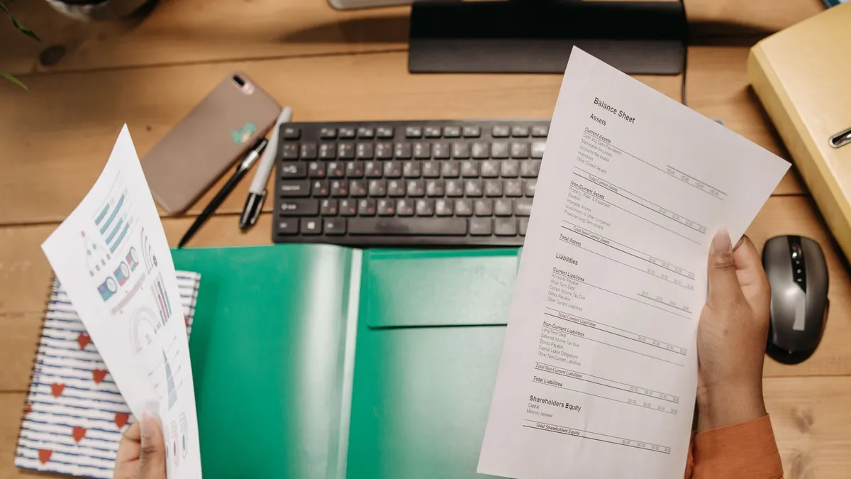 Hands holding and reviewing balance sheets over a desk with a keyboard and stationery.