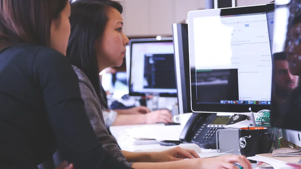 Two women working together on code at a computer in a modern office setting.