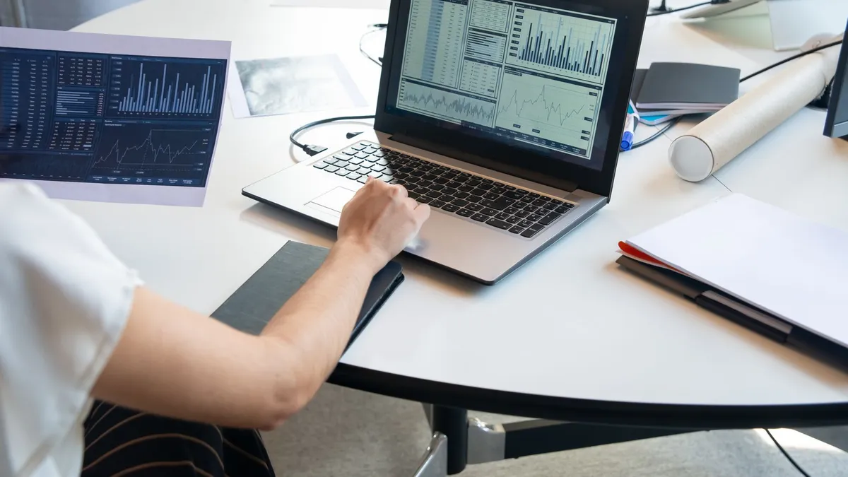 Business person evaluating financial charts on a laptop in a modern office setting.