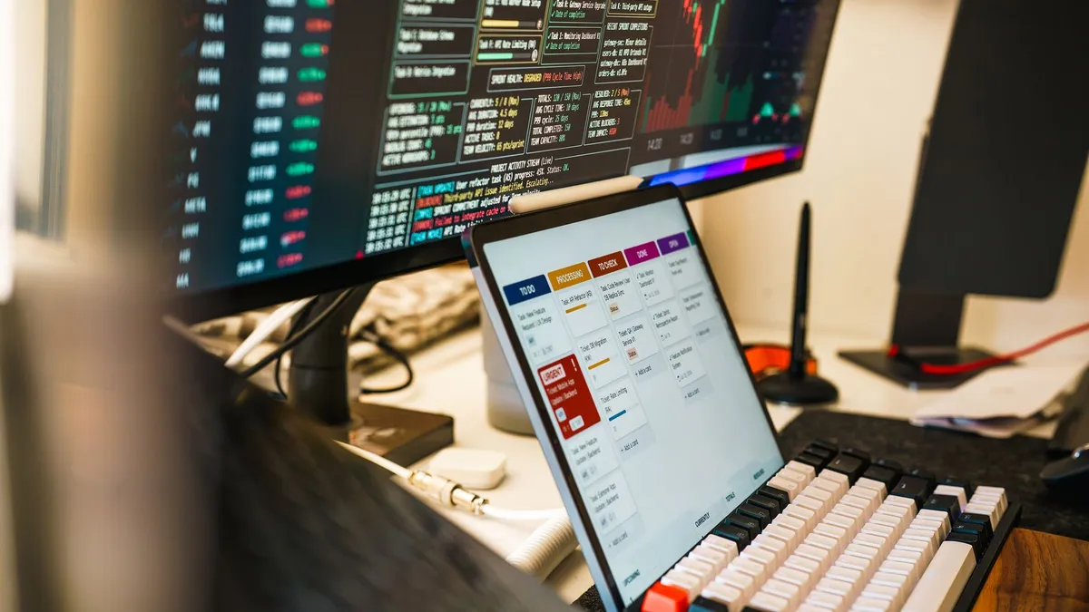 A sleek, modern workspace featuring trading monitors and a tablet for project management.