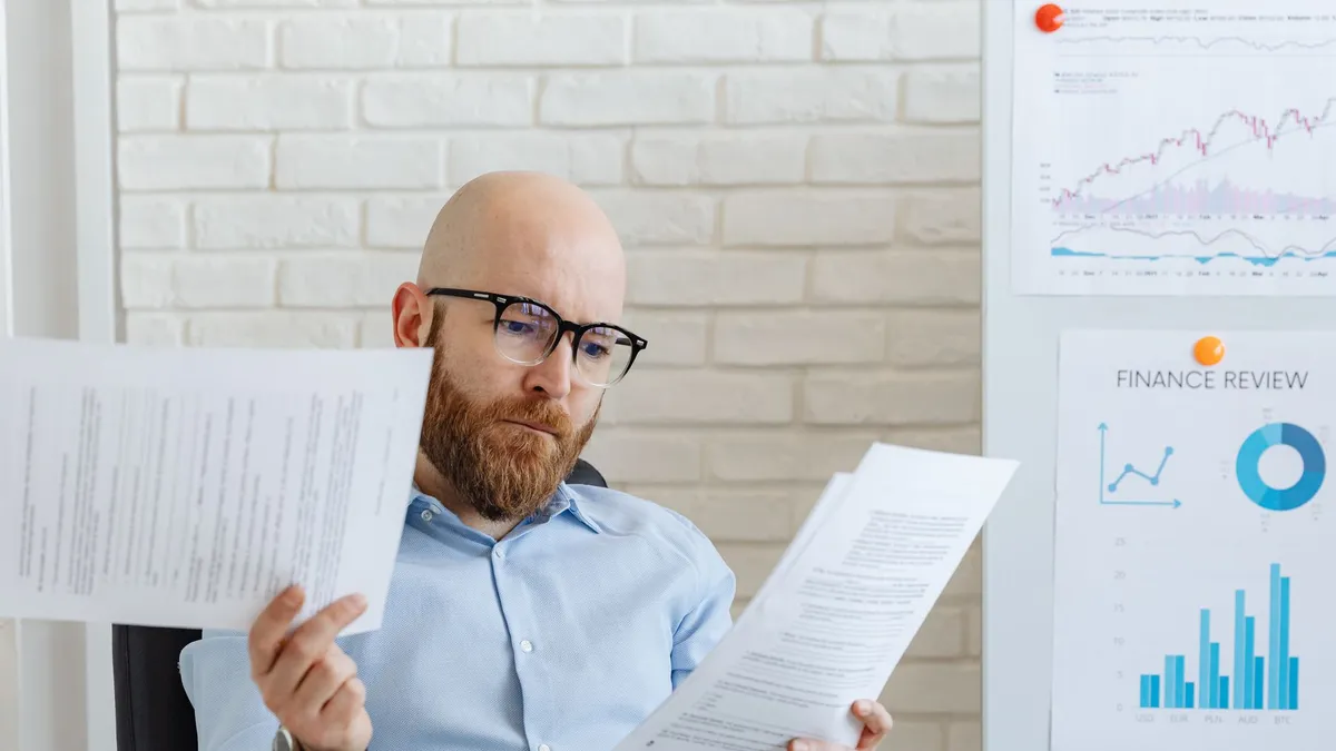 Bald bearded businessman reading financial documents in modern office setting.