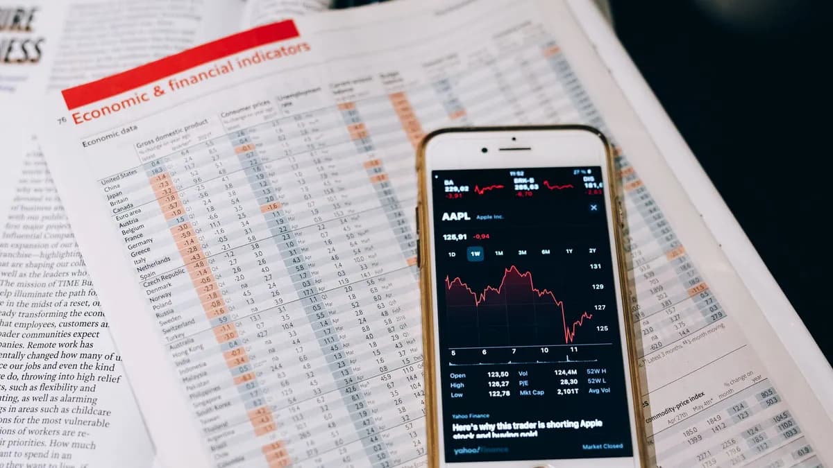 Smartphone displaying stock market data on papers with financial charts.