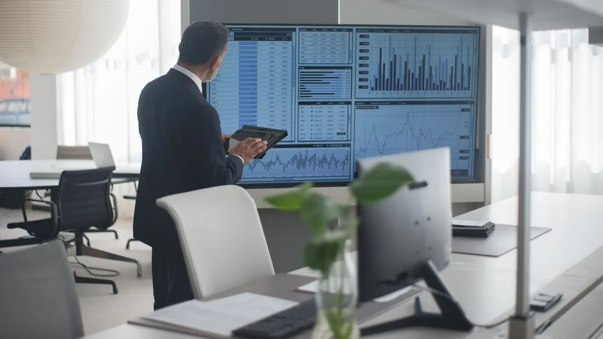 Professional in suit analyzing financial data on screens in a modern office setting.
