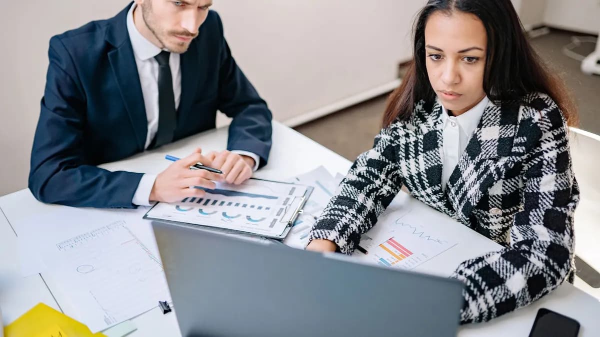A man and woman collaborate on business analysis at a desk with charts in an office setting.