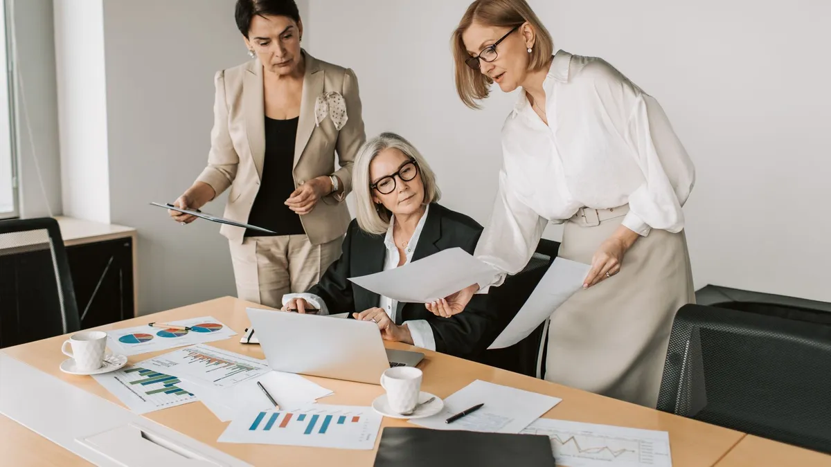 Three businesswomen discussing reports in a modern office environment.