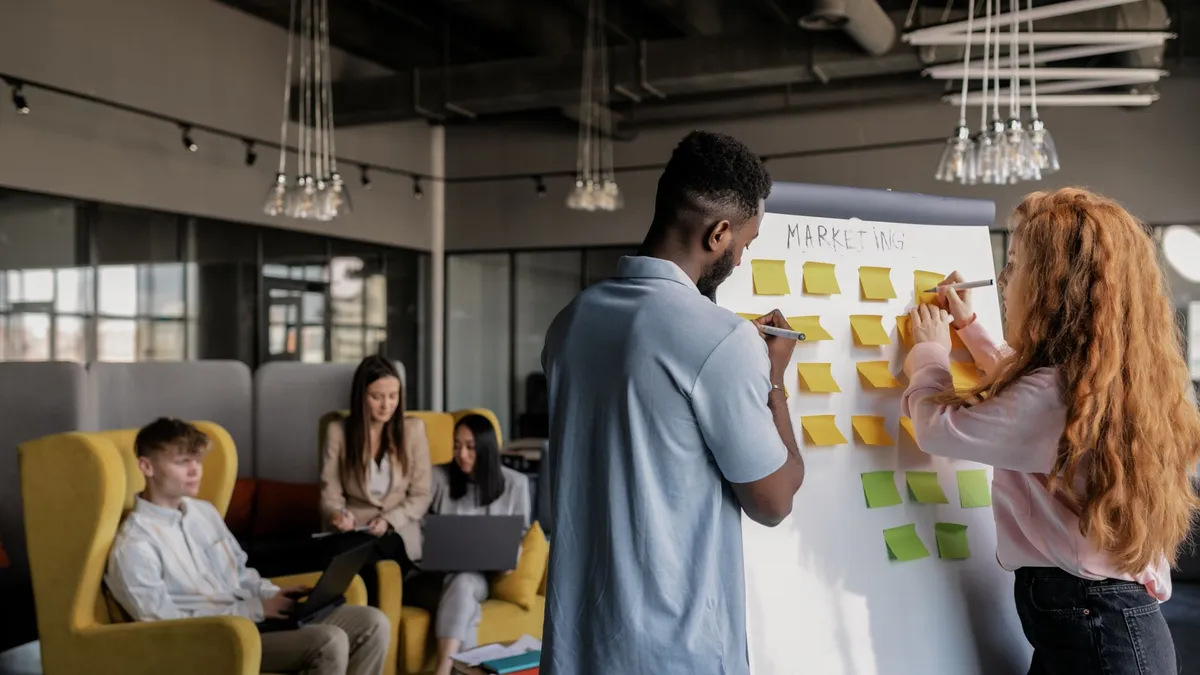 Team collaborating in a modern office, planning strategy on a whiteboard, young adults working together.