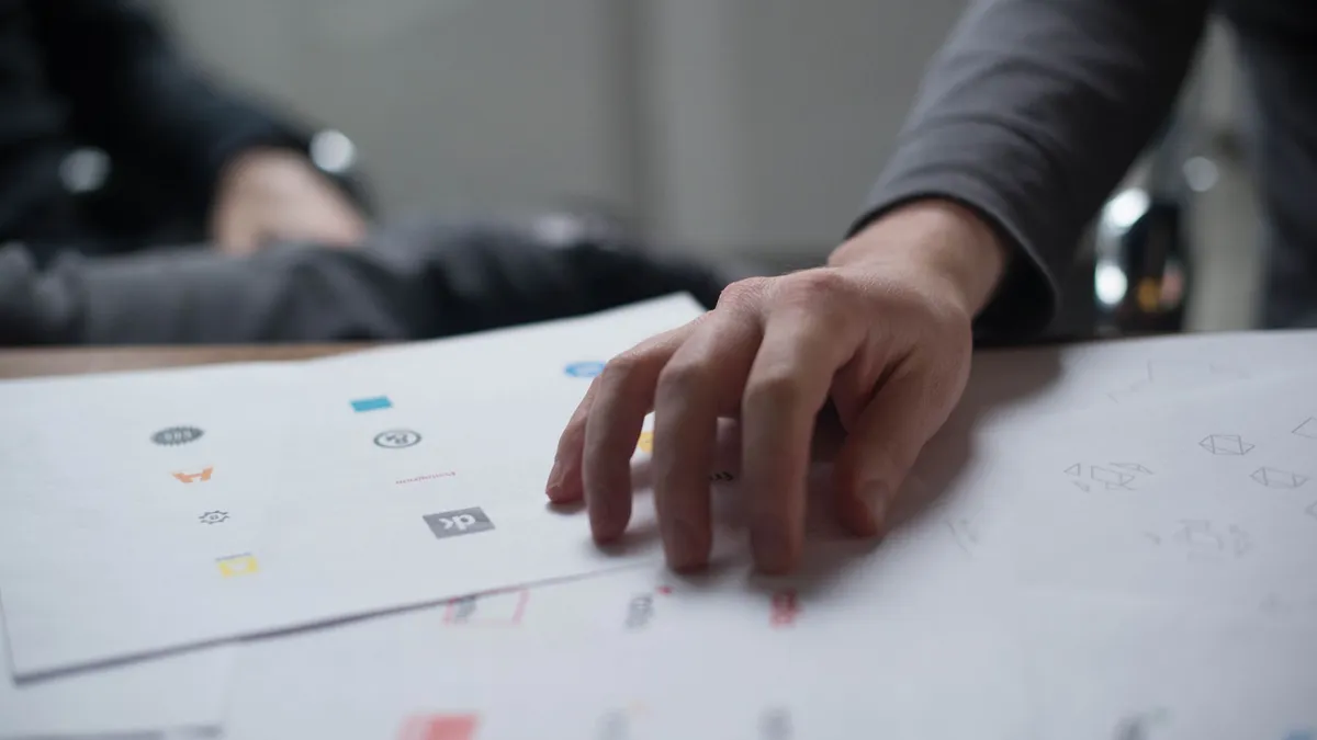 A close-up shot of a hand reviewing various logo designs on paper, ideal for business concepts.
