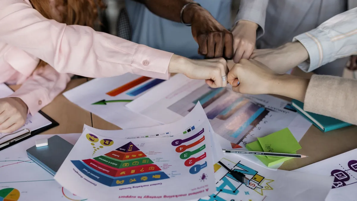 A diverse team unites hands over business reports and marketing strategies, symbolizing teamwork.