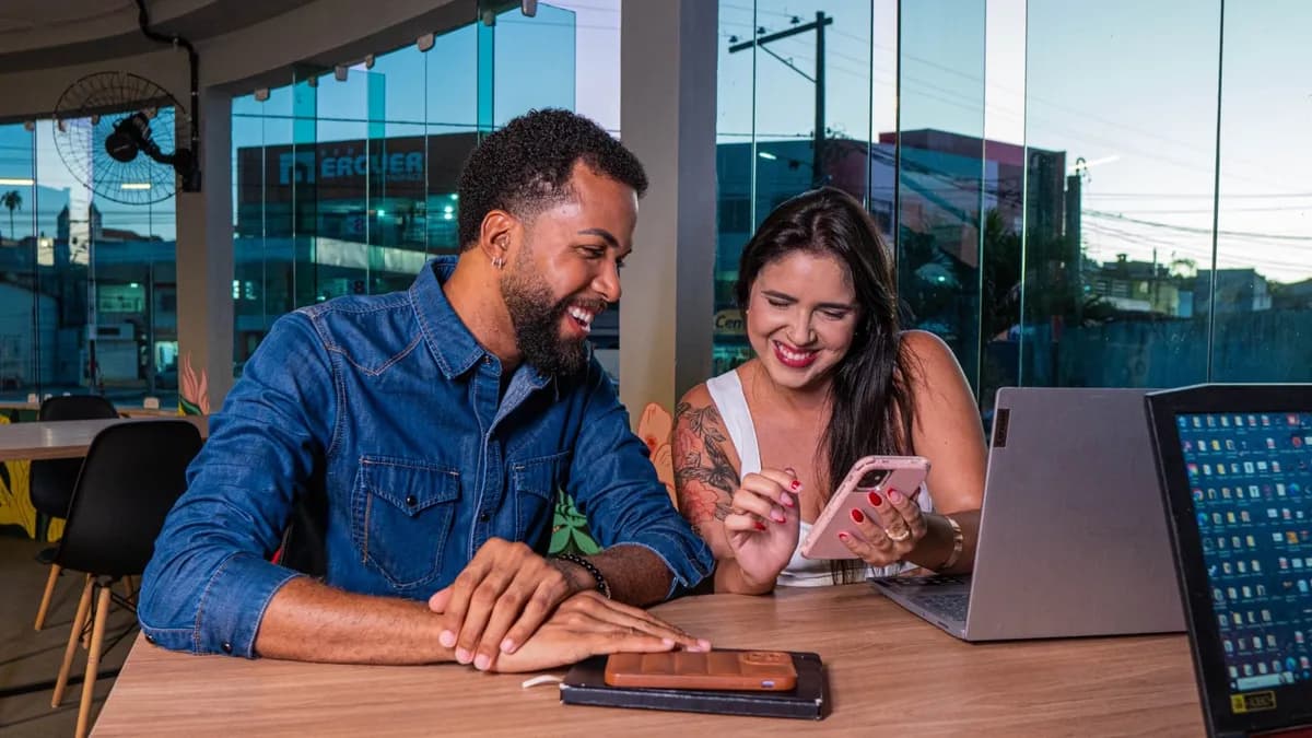 Two colleagues enjoying work at a modern office, using a smartphone and laptop.