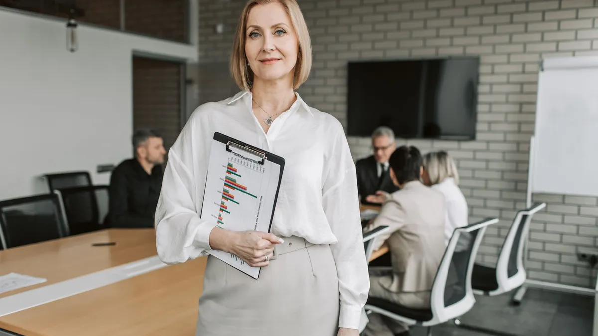 Professional businesswoman holding a clipboard during an office meeting, showcasing leadership in a corporate environment.