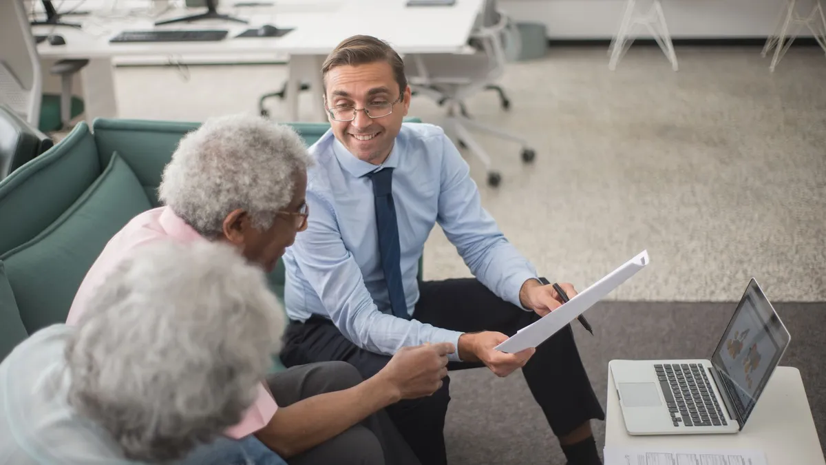 Consultant discussing financial plans with senior clients in a modern office setting, using documents and a laptop.