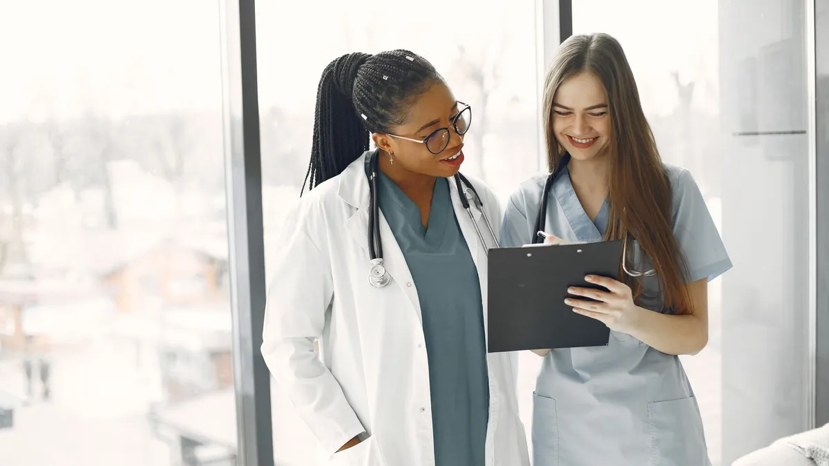 Two female healthcare professionals discussing documents in a bright medical setting.