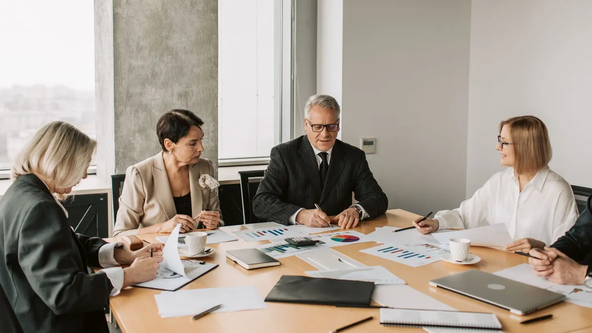A group of professionals discussing business documents during a meeting in a modern office setting.