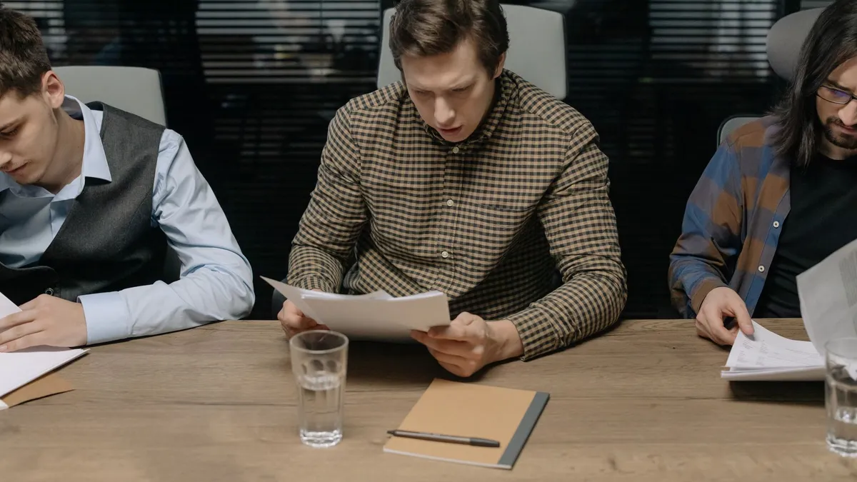 Three men reviewing papers in a modern office setting during a business meeting.
