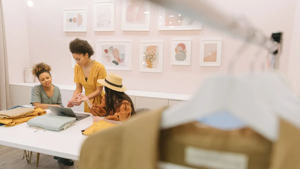Three women engaged in brainstorming session with fabrics and laptop in a stylish fashion studio.