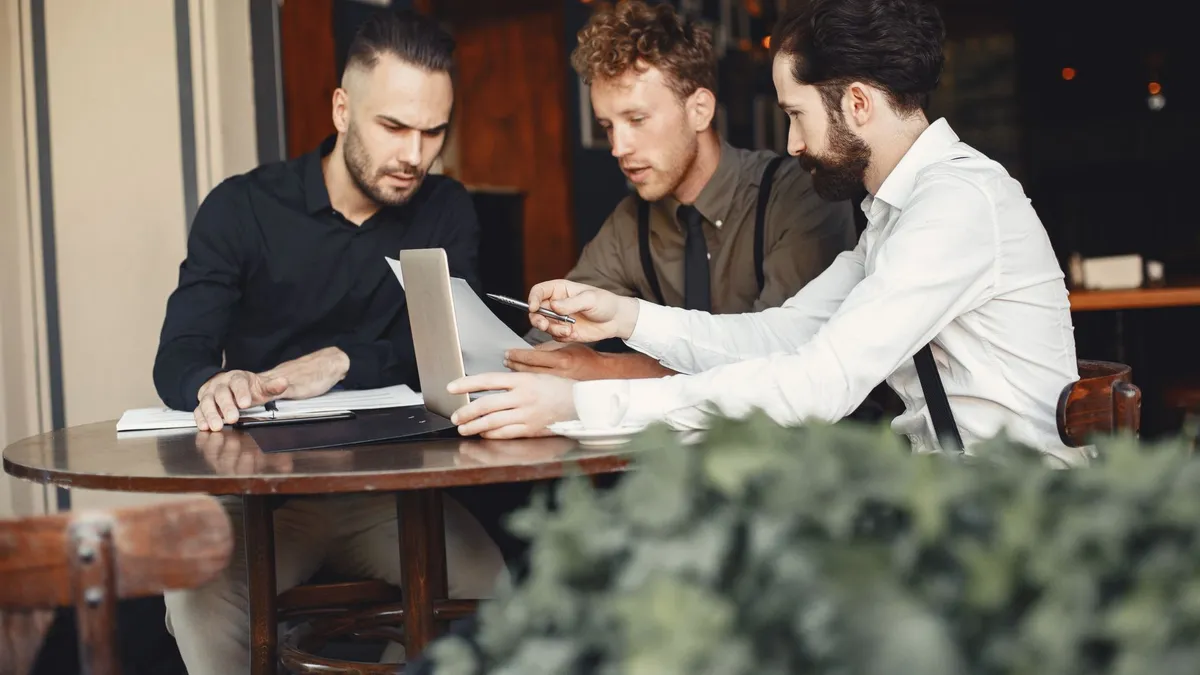 Three young men collaborating in a cozy cafe setting, focused on a laptop.