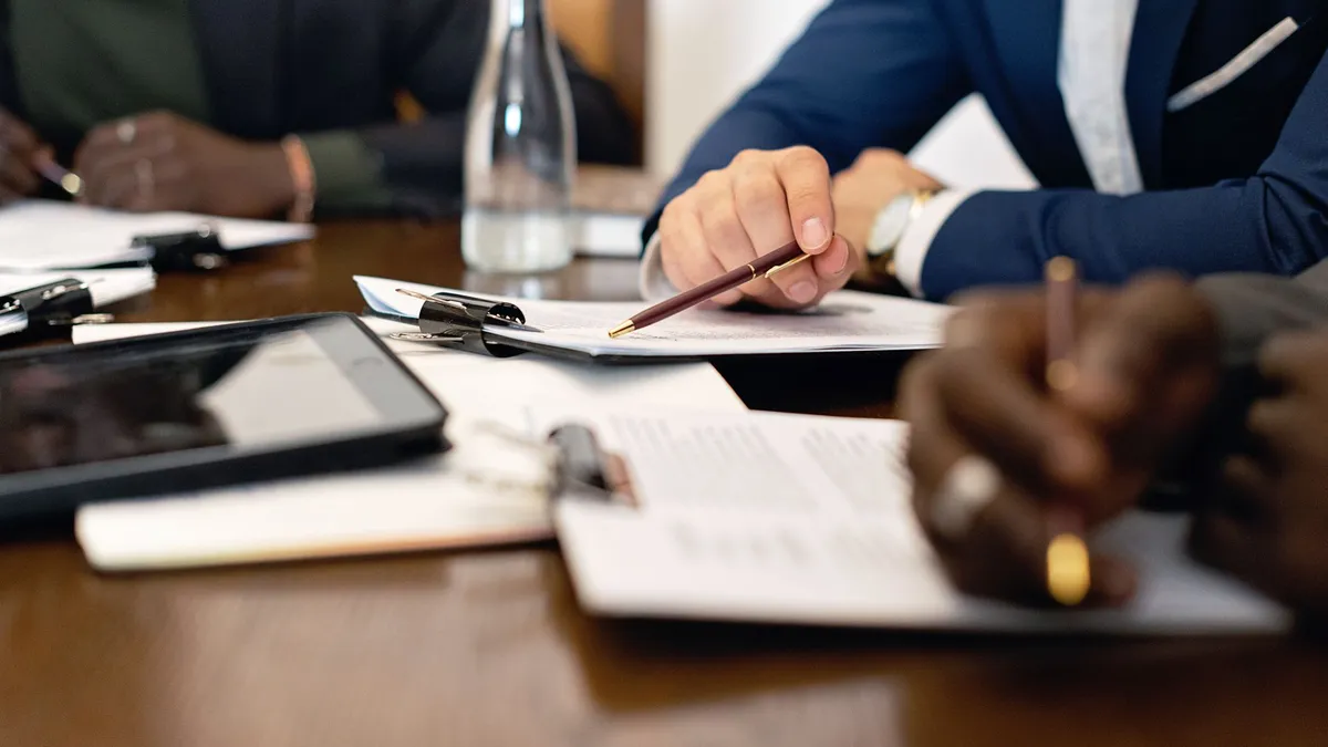 Business meeting with adults discussing and signing contracts over a table.