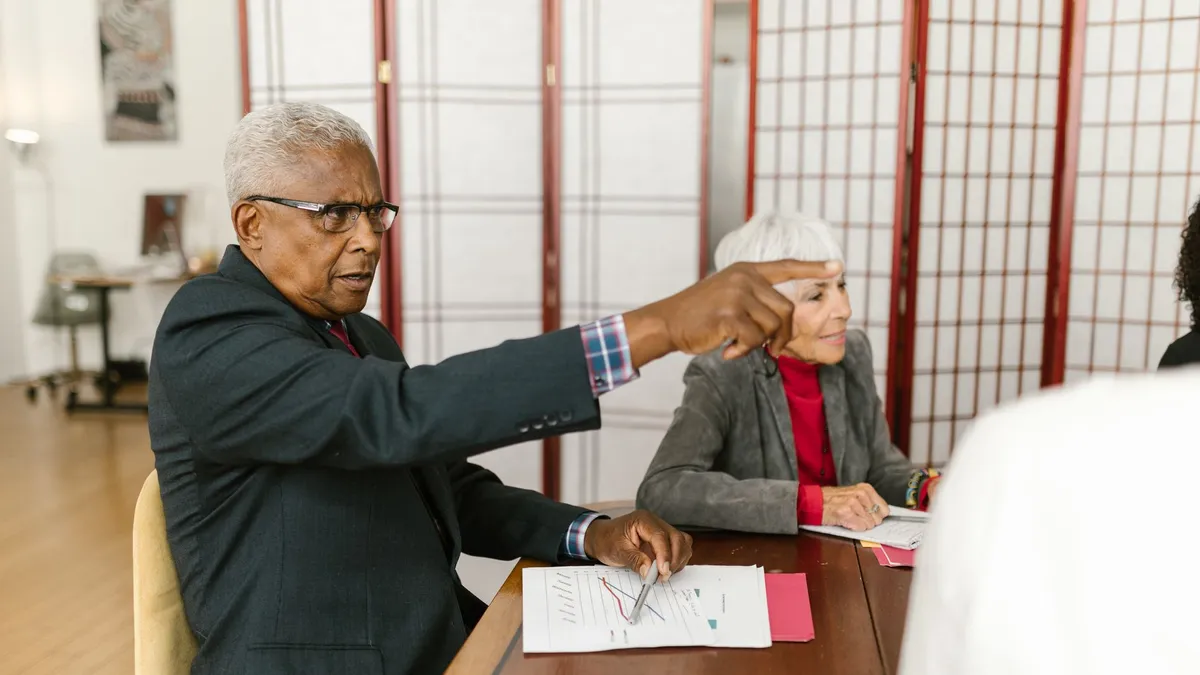 Elderly professionals collaborate in a meeting, discussing documents on a wooden table.