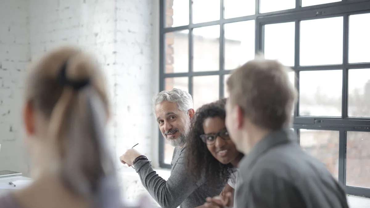 Cheerful diverse employees of different ages in casual wear having pleasant informal conversation while sitting together at table in office boardroom