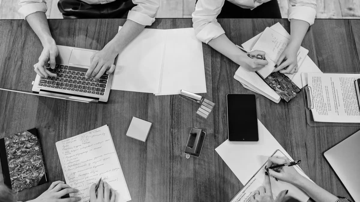 Top view of team members working together on a wooden table, using various office tools.