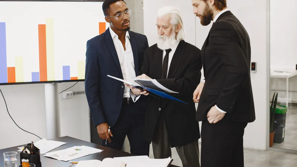 Three businessmen in suits discussing reports in a modern office setting.