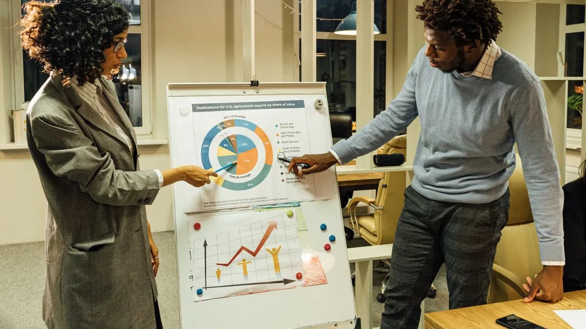 Two professionals engaged in a business meeting discussing charts on a whiteboard in a modern office.
