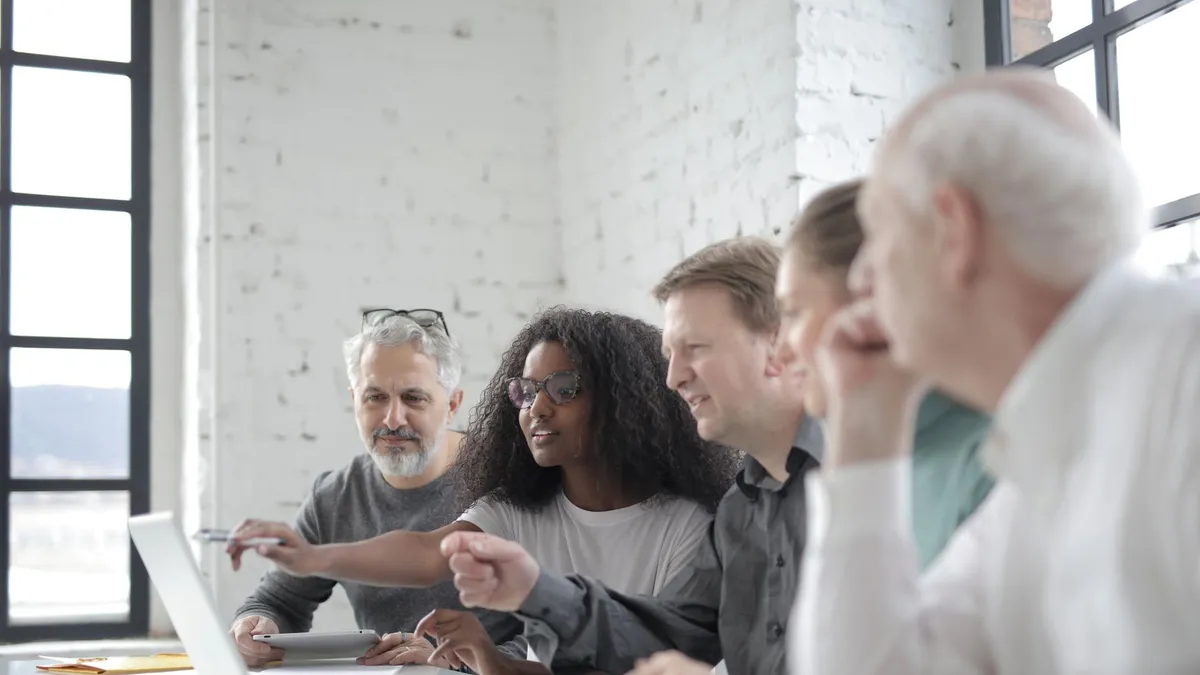 Content African American female worker pointing at netbook screen while speaking about project with diverse colleagues and sitting at white table in office in sunlight