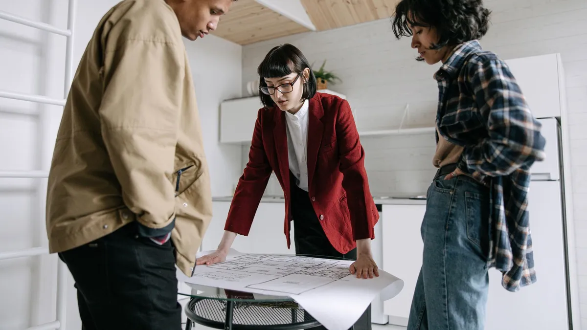 A real estate agent discusses property plans with a young couple indoors.