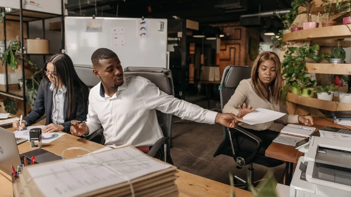 A group of colleagues working together in a modern, plant-filled office, discussing documents.