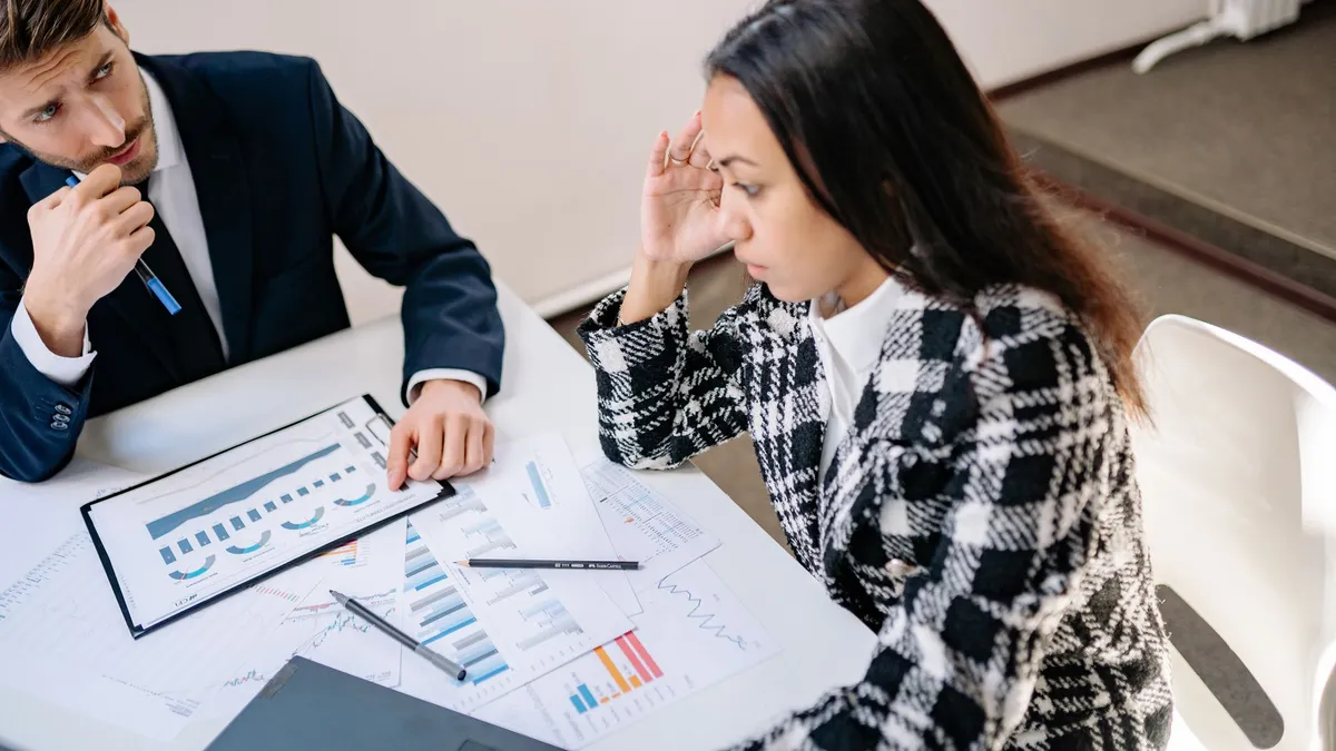 Two colleagues discussing graphs and charts during a business meeting indoors.