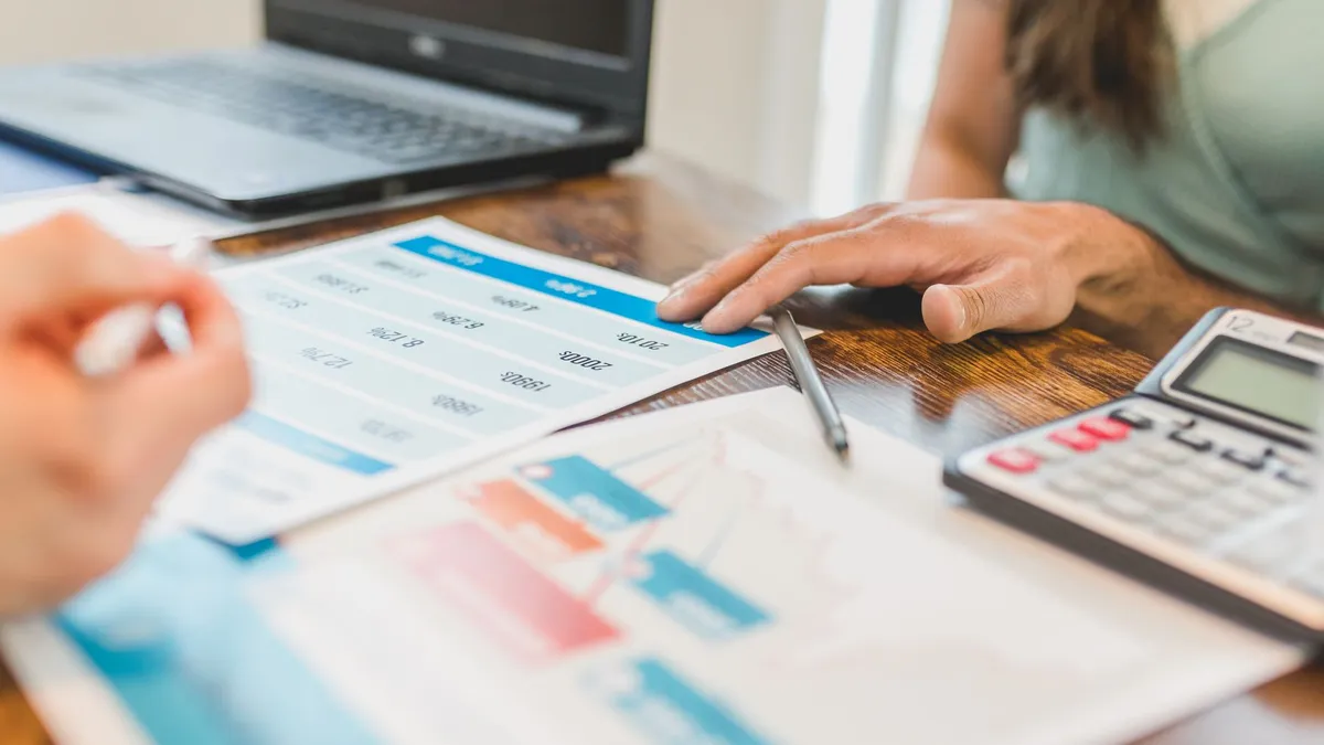 Hands at a desk with financial graphs, calculator, and pen, analyzing business data.
