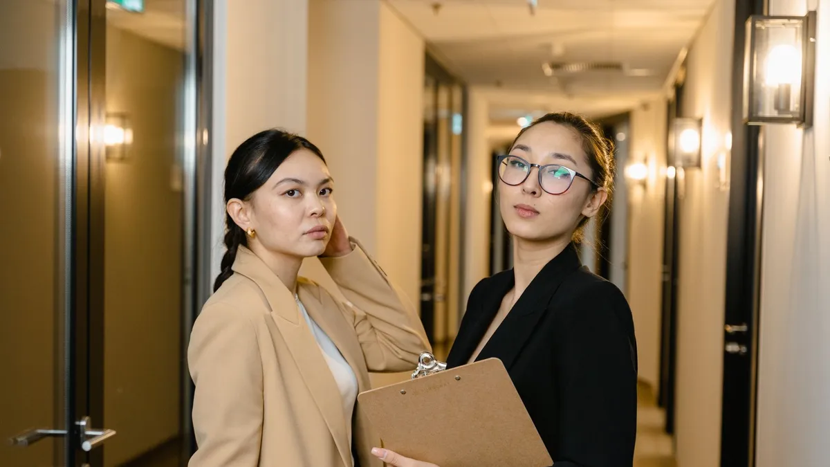 Two professional women in suits standing confidently in an office hallway.