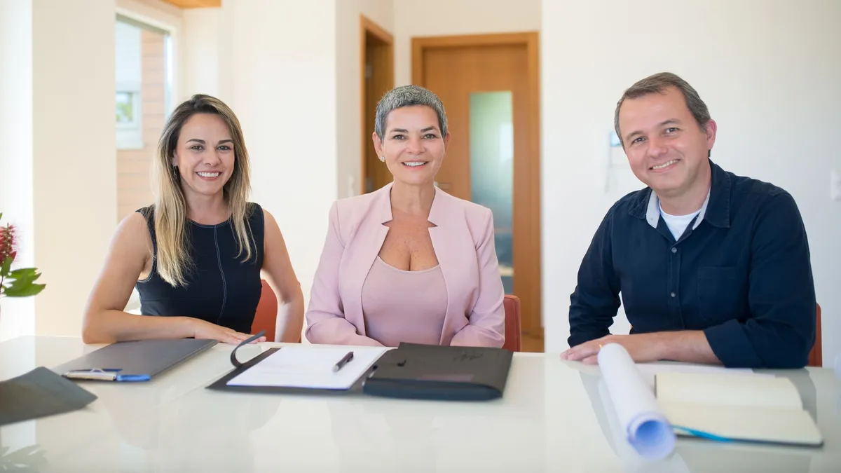 Three professionals smiling at a business meeting in a modern office.