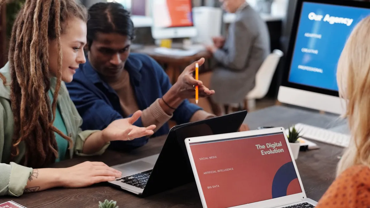 Diverse team collaborating with laptops in a modern office setting, discussing digital evolution.