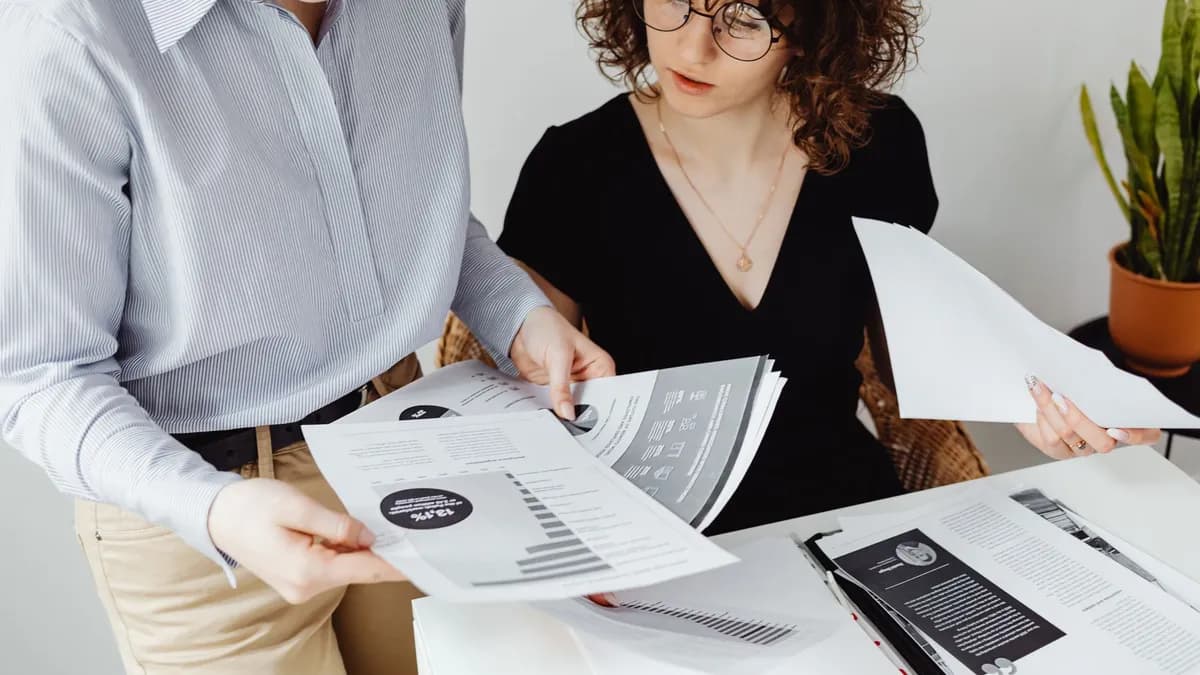 Two women review and discuss financial documents in an office setting, highlighting teamwork and analysis.