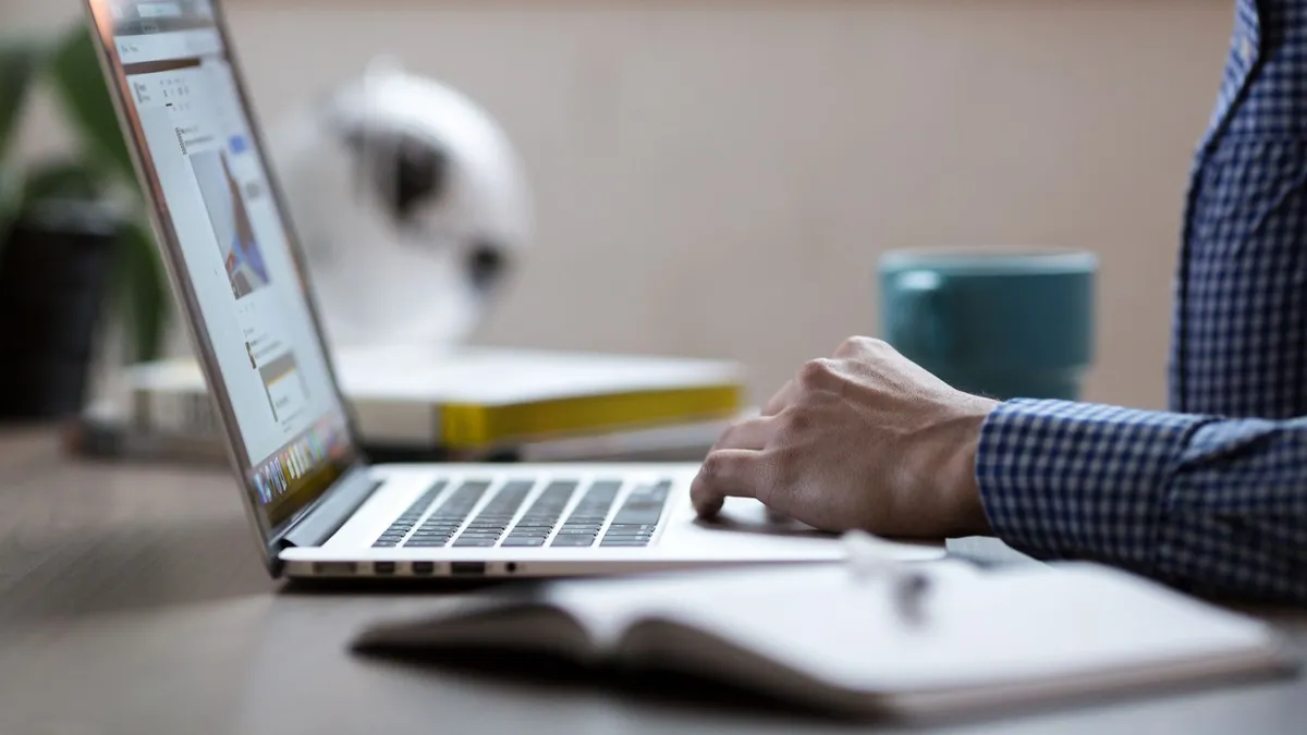 Business professional working on laptop at an office desk with coffee mug.