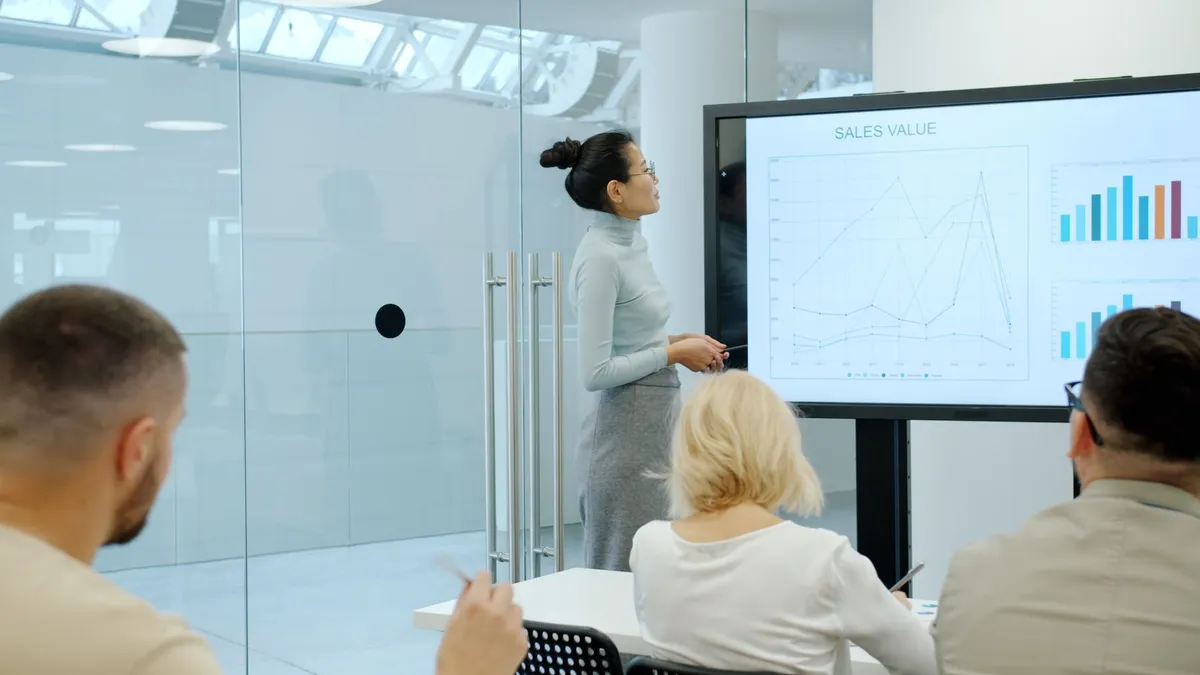 Businesswoman presents sales data to colleagues in a modern office.