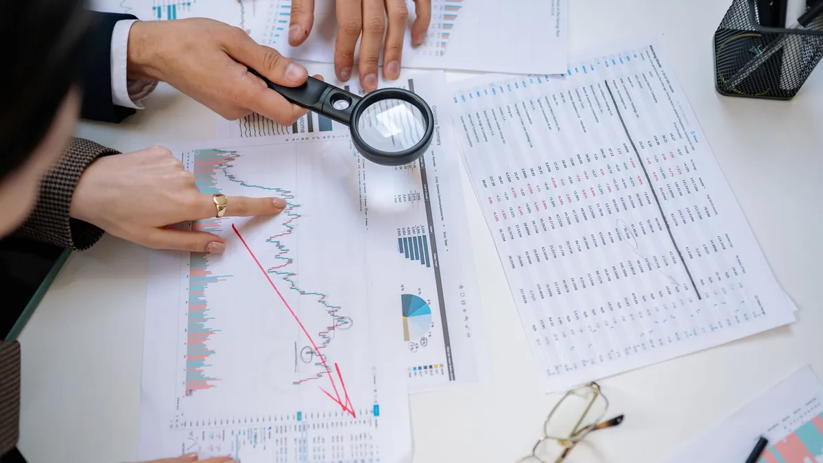 Business professionals examining financial documents with magnifying glass for detailed analysis.
