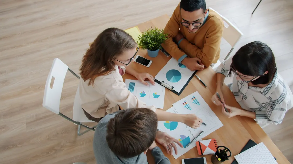 A top view of a team of adults collaborating on business analytics at a wooden table.